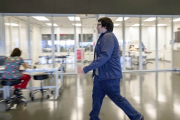Lucas Grijalva walks across the open floor of ASTEC while a woman in the backgound hunches over a computer.