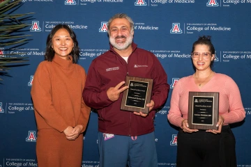 Three smiling UArizona College of Medicine – Tucson faculty members, two of whom are holding plaques, pose for a photo.