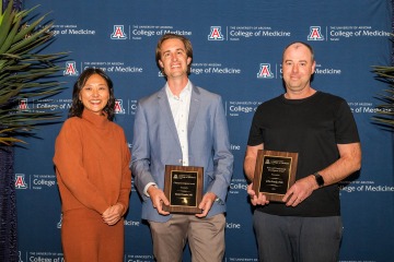 Three smiling UArizona College of Medicine – Tucson faculty members, two of whom are holding plaques, pose for a photo.