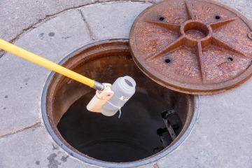 a plastic bottle attached to a long pole is lowered into the sewer through an open manhole