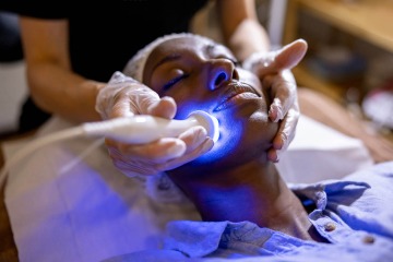 A dermatologist uses ultrasound and light therapy rejuvenation treatment on a woman’s face.