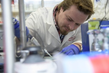 man leaning over a table and using a pipette in a research laboratory