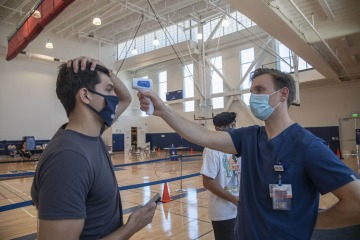 a person taking another person’s temperature by pointing a laser thermometer at their forehead 