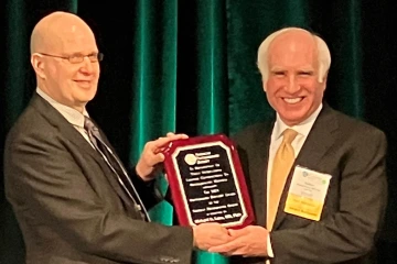 One man presents a plaque award to another man.