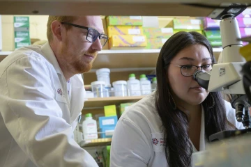 Angel-Grace Charity Leslie looking at microscope with mentor over shoulder