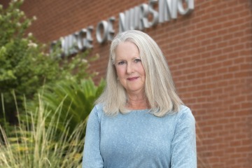 Portrait of professor Melissa Goldsmith wearing a light-blue blouse in front of the University of Arizona College of Nursing building.