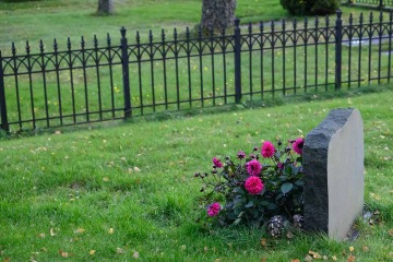 a headstone and flowers are surrounded by green grass at a cemetary with a black picket fence in the background