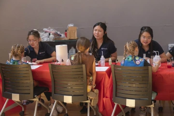 Three pharmacy students sit at a table each facing a Girl Scout doing an activity with them.