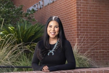 Portrait of Timian Godfrey in front of the College of Nursing, smiling, wearing a black shirt and turquoise necklace.