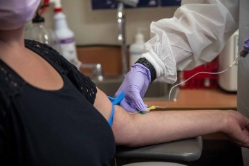 Close-up shot of a woman looking at her arm while a gloved hand holds a needle against it.