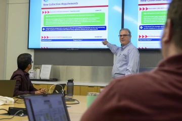 Dr. Justin Starren stands and points at a large screen in a conference room