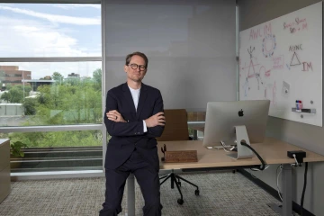 Stephen Dahmer, MD, sits on the edge of his desk in his office.