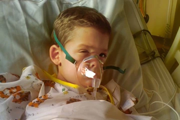 young child wearing an oxygen mask in a hospital bed