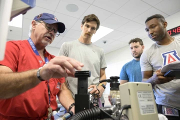 Professor Jim Reed demonstrates how to use medical equipment to three students in a simulation lab. 