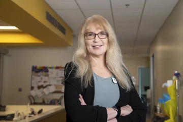 Janine Hinton, PhD, stands with her arms crossed in front of the nurses station in the Gilbert simulation center.