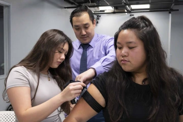 Jonathan Lee-Confer assists a student putting an arm sensor on another student.