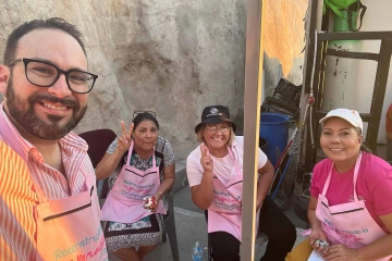 Four smiling people wearing pink aprons posing for a selfie at a breast cancer fundraiser