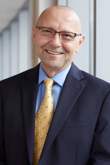 Portrait of physician-scientist Dr. Dan Theodorescu wearing a dark blue suit with yellow tie