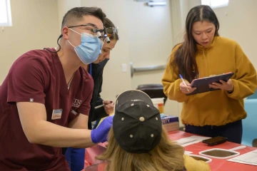 Dental students perform a dental screening with an attendee at a health and dental fair 