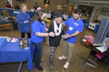 Two students assist an older woman at a falls prevention demonstration at a health fair.