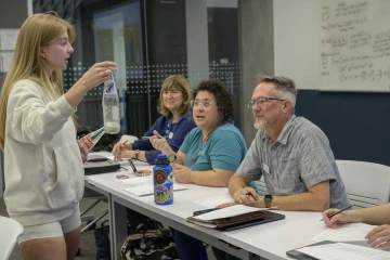 A student practices her presentation while standing in front of faculty members, who are seated.