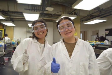 Two female med-start students smiling and holding their thumbs up.