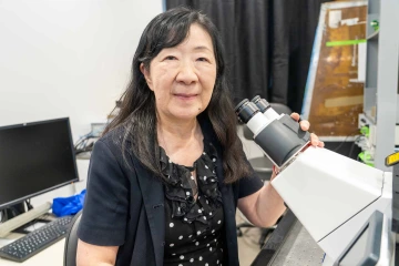 Nipavan Chiamvimonvat, MD, is seated in a lab with her left hand on a microscope