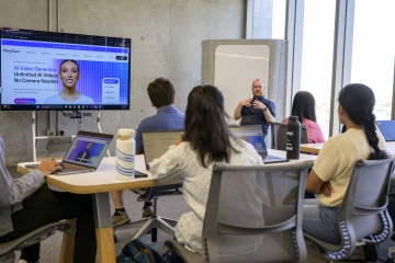 A professor talking to students sitting at tables in a classroom with laptops