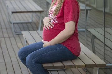 Pregnant person sitting on bench and resting hand wearing smart ring on first finger on belly