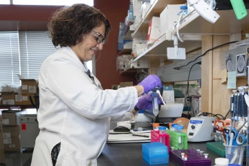 Fariba Donovan, MD, PhD, in a lab wearing purple gloves on her hands and holding lab equipment.