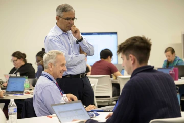 Nirav Merchant, director of the University of Arizona’s Data Science Institute, stands with his hand at his mouth looking at a screen while Marvin Slepian, MD, JD, is smiling and seated next to him.