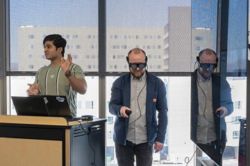 professor wearing VR goggles reviews a student’s VR project