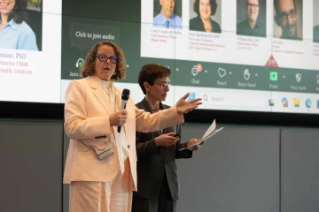 Several people stand in front of a seated audience as they present a proposal which is projected on a screen behind them.