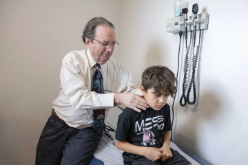 A doctor conducting an exam on a boy sitting on a medical exam table.