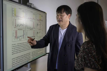 Faculty mentor points to graphs on a large digital display while talking to graduate student