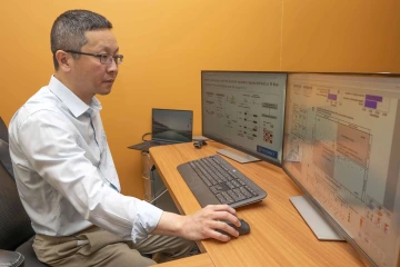 Mingyu Liang, MB, PhD, sits at a desk with his hand on a mouse, staring at two computer monitors in front of him.