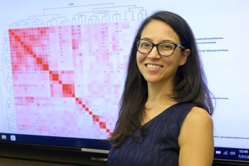 Portrait of Melissa Furlong, PhD, standing in front of a pink and red graph on a large digital display