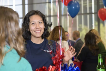 Photo of a smiling young woman with red and blue balloons in the background.