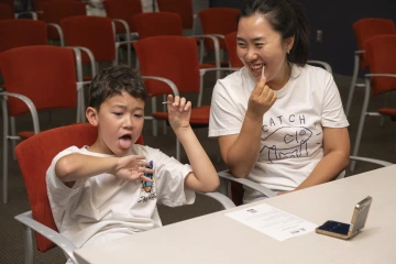 A young boy sitting next to his smiling mom sticks his tongue out.