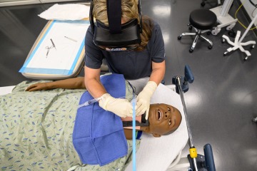 student practices a medical procedure on a mannikin while using virtual reality headset