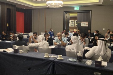 People sitting at tables at a conference in Abu Dhabi, UAE. Half of the group are wearing surgical masks.
