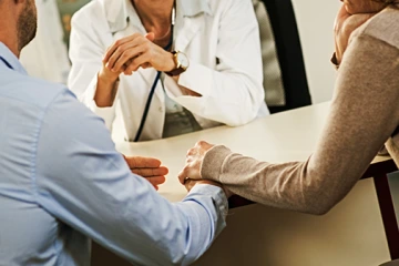 Worried couple holding hands while listening to female doctor.