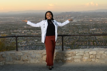 Black woman stands with outstretched arms overlooking a city