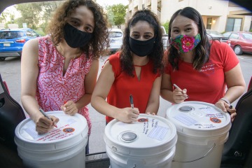 Nicole Bejany, Guadalupe Davila and Thomasina Blackwater, students in the College of Medicine – Tucson, write well-wishes on 5-gallon buckets of hand sanitizer before distributing them on the Navajo Nation. 