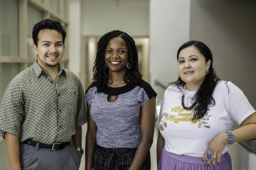 A man and two women stand together smiling.