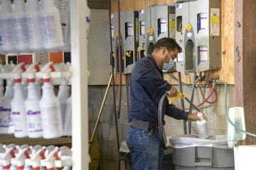 Grounds crew chief Humberto Sarabia-Fulgencio refills a bottle of Oxivir disinfectant in Facilities Management’s converted Small Engine Shop, now a disinfectant station. The station refills thousands of bottles of disinfectant to share across the campuses.