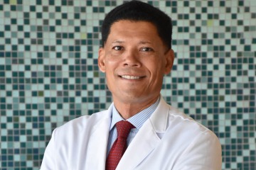 Man wearing a medical white coat stands smiling