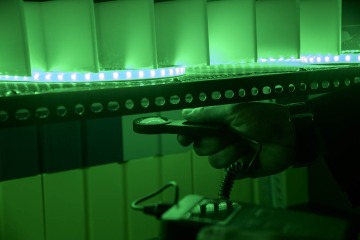a hand holds a light meter under a strand of green led lights