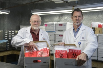 David Harris, PhD, MS, director of the University of Arizona Biorepository, and Michael Bawdowski, PhD, associate research scientist, hold boxes of COVID-19 sample collection kits ready for use in health care facilities.