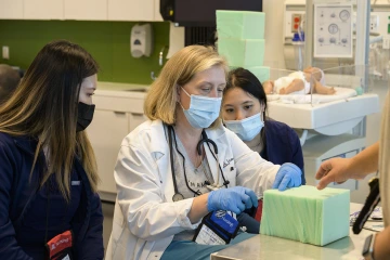 professor showing two students how to perform a clinical procedure during a simulation exercise